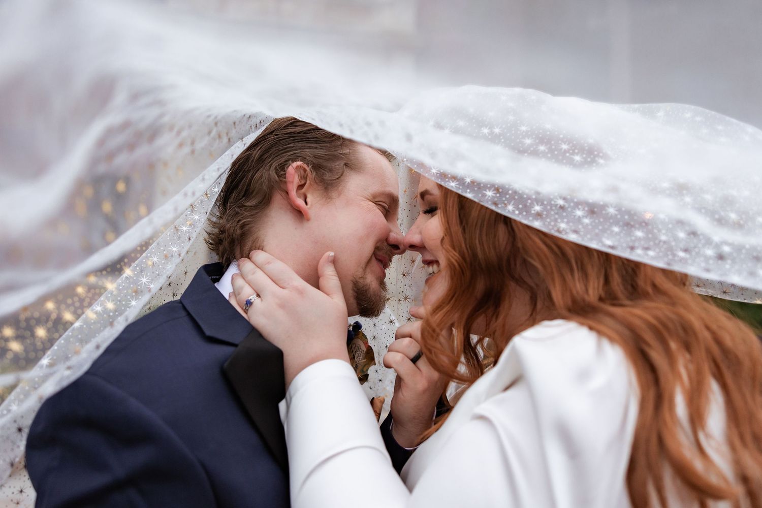 Bride and groom sharing romantic moment under sparkle veil.