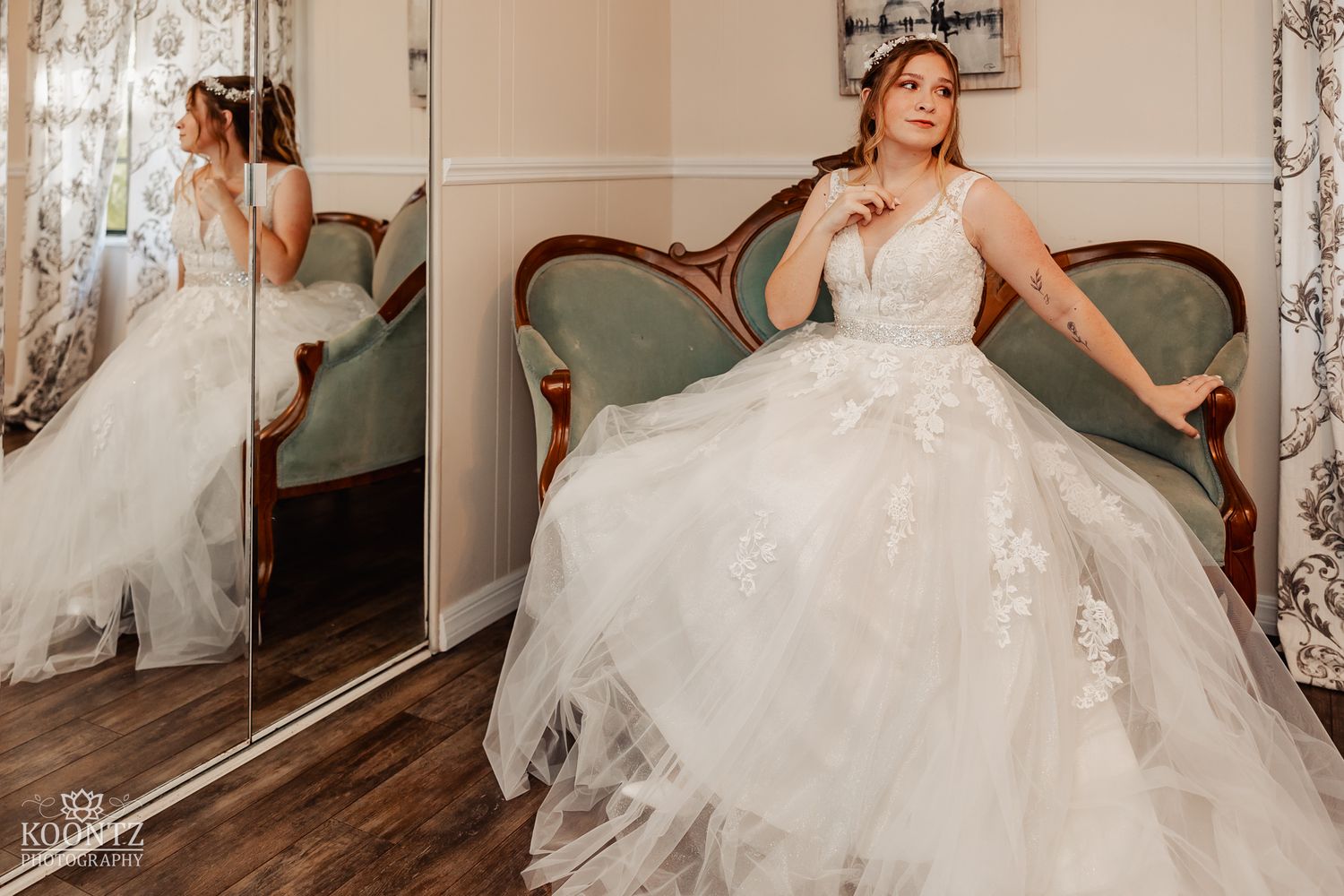 Bride in a full tulle ball gown poses elegantly on a vintage sofa beside a mirror reflection.