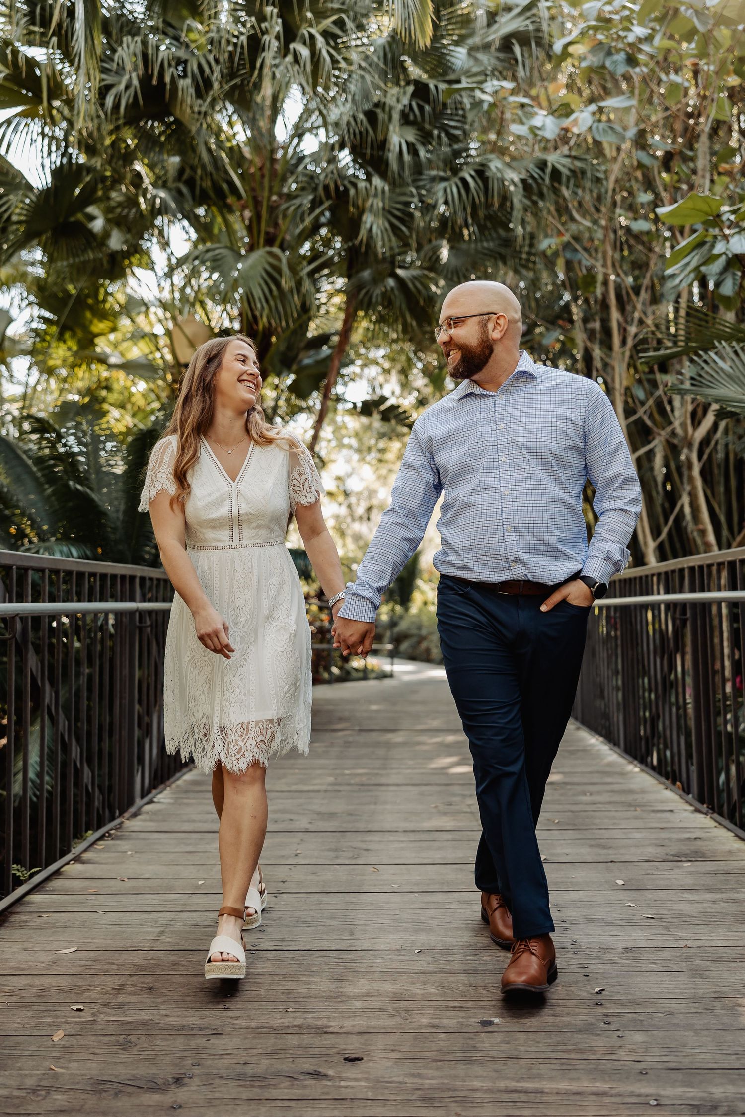 Happy couple walking hand in hand across a wooden bridge surrounded by lush tropical greenery.