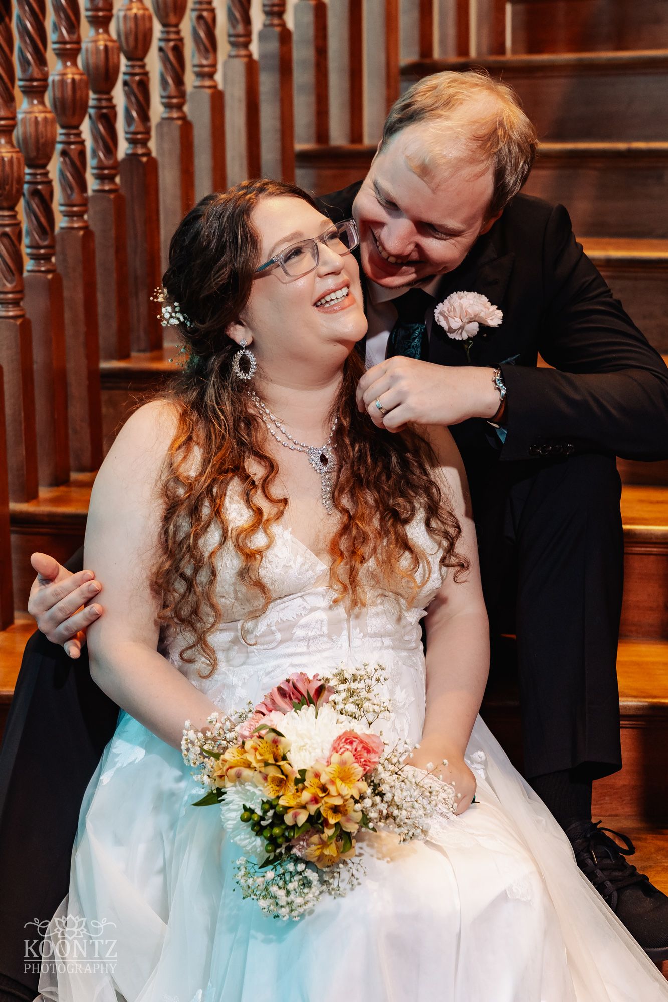 A joyful wedding moment captured on wooden stairs with long curly hair and bridal bouquet in autumn colors.