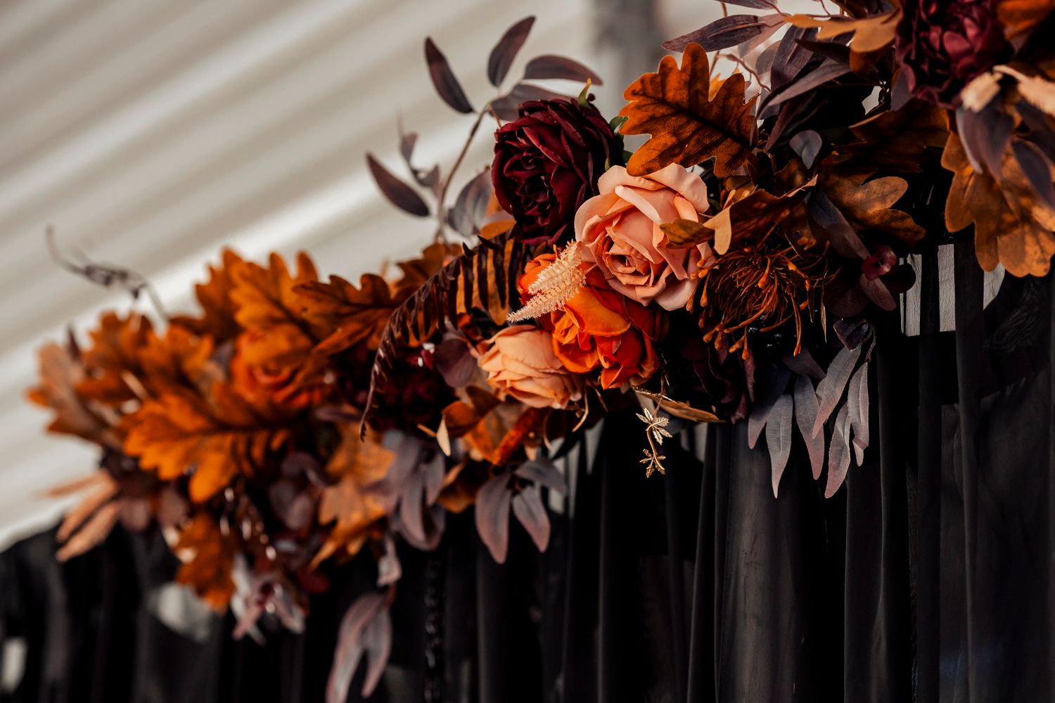 Autumn-themed floral arrangement with burgundy and orange blooms against a dark backdrop.