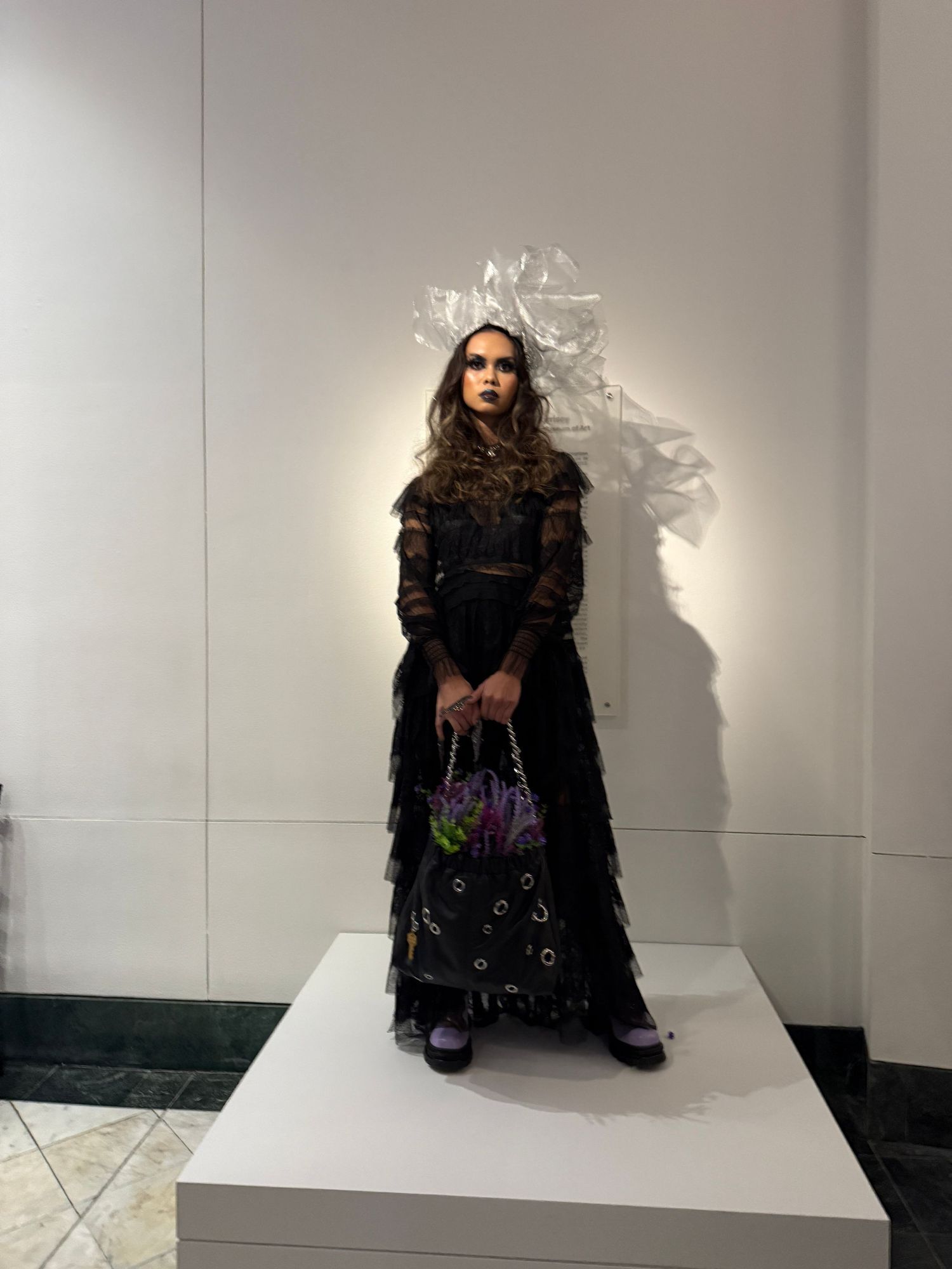 A series of five fashion photos showing a model in a black coat and white headpiece against a white studio backdrop.