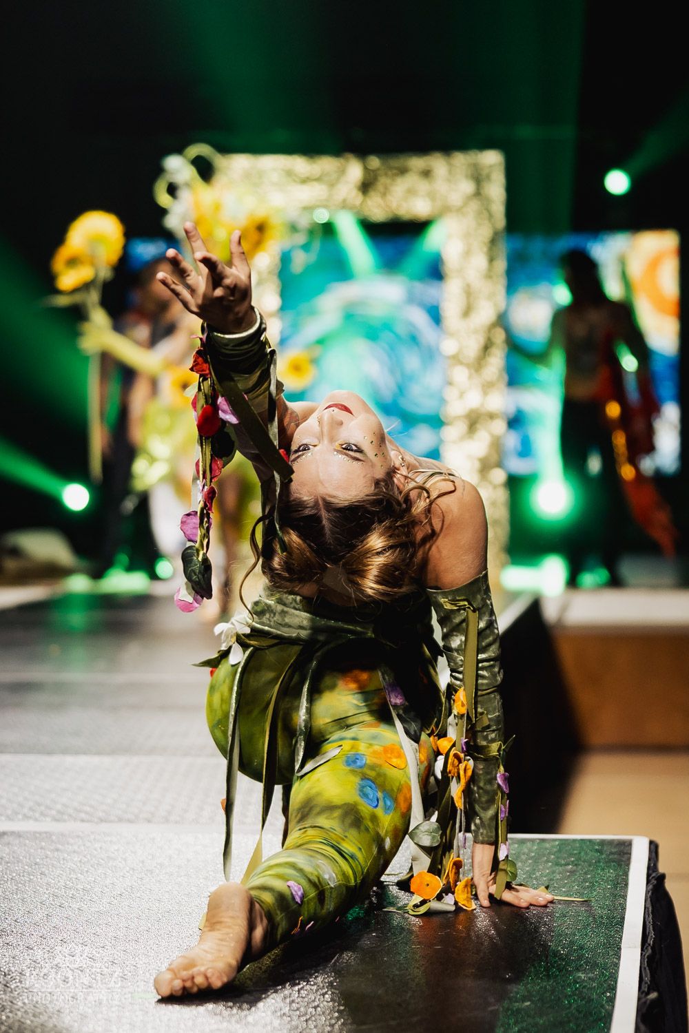Artistic performance featuring green military-style costumes and props on stage with emerald lighting.