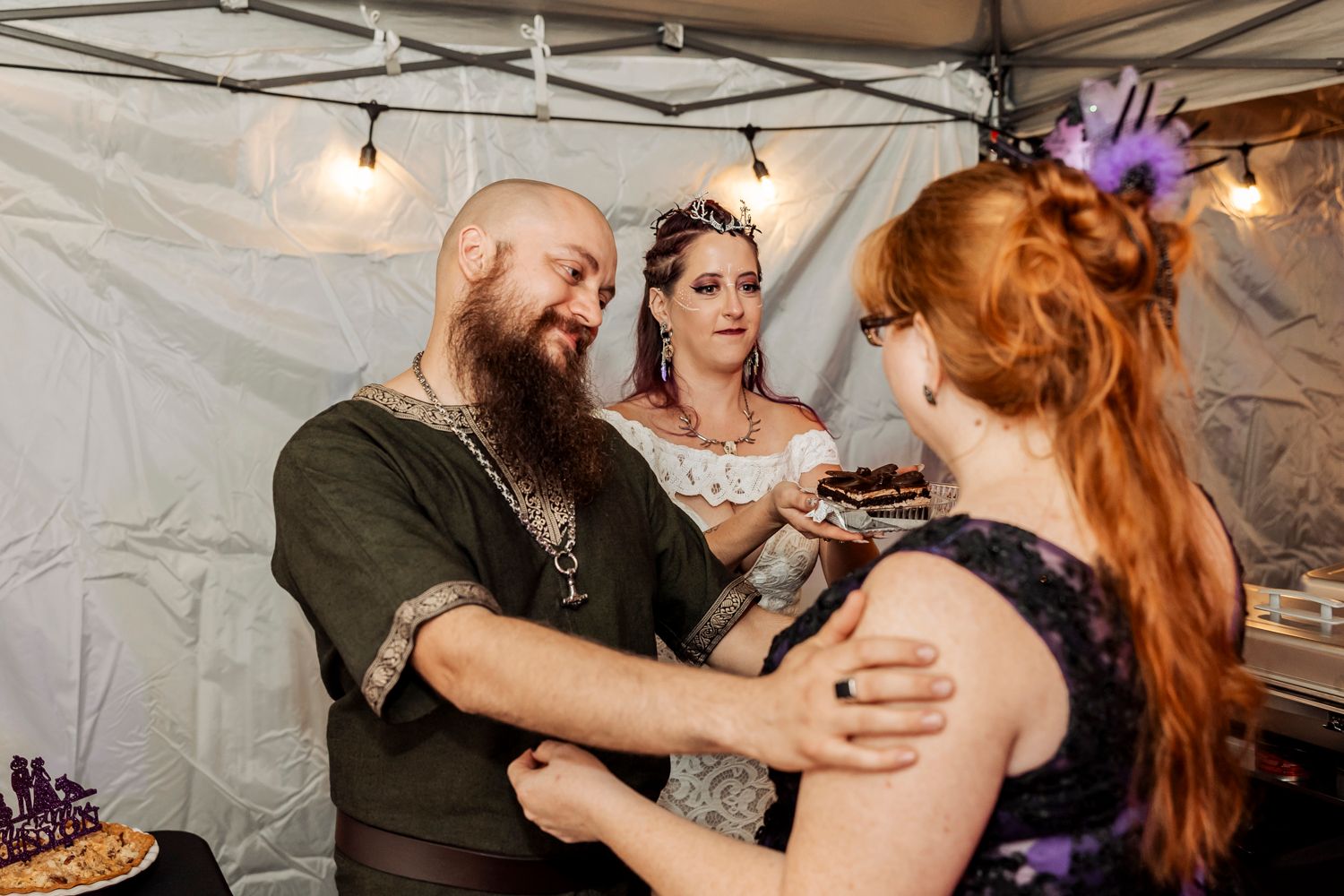 Wedding reception moment with guests sharing desserts under string lights and white tent.