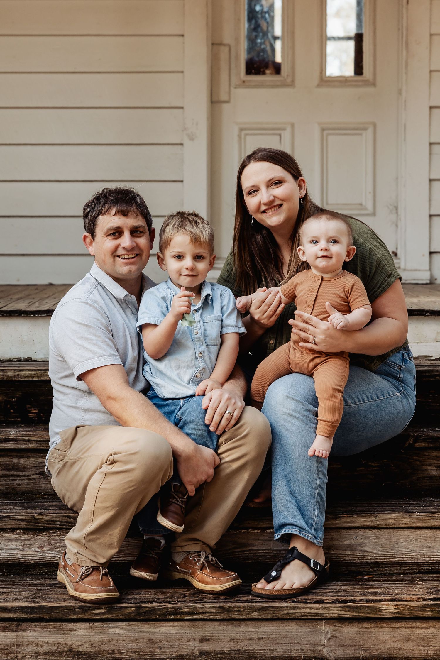 Happy family of four posing on wooden porch steps with two young children.