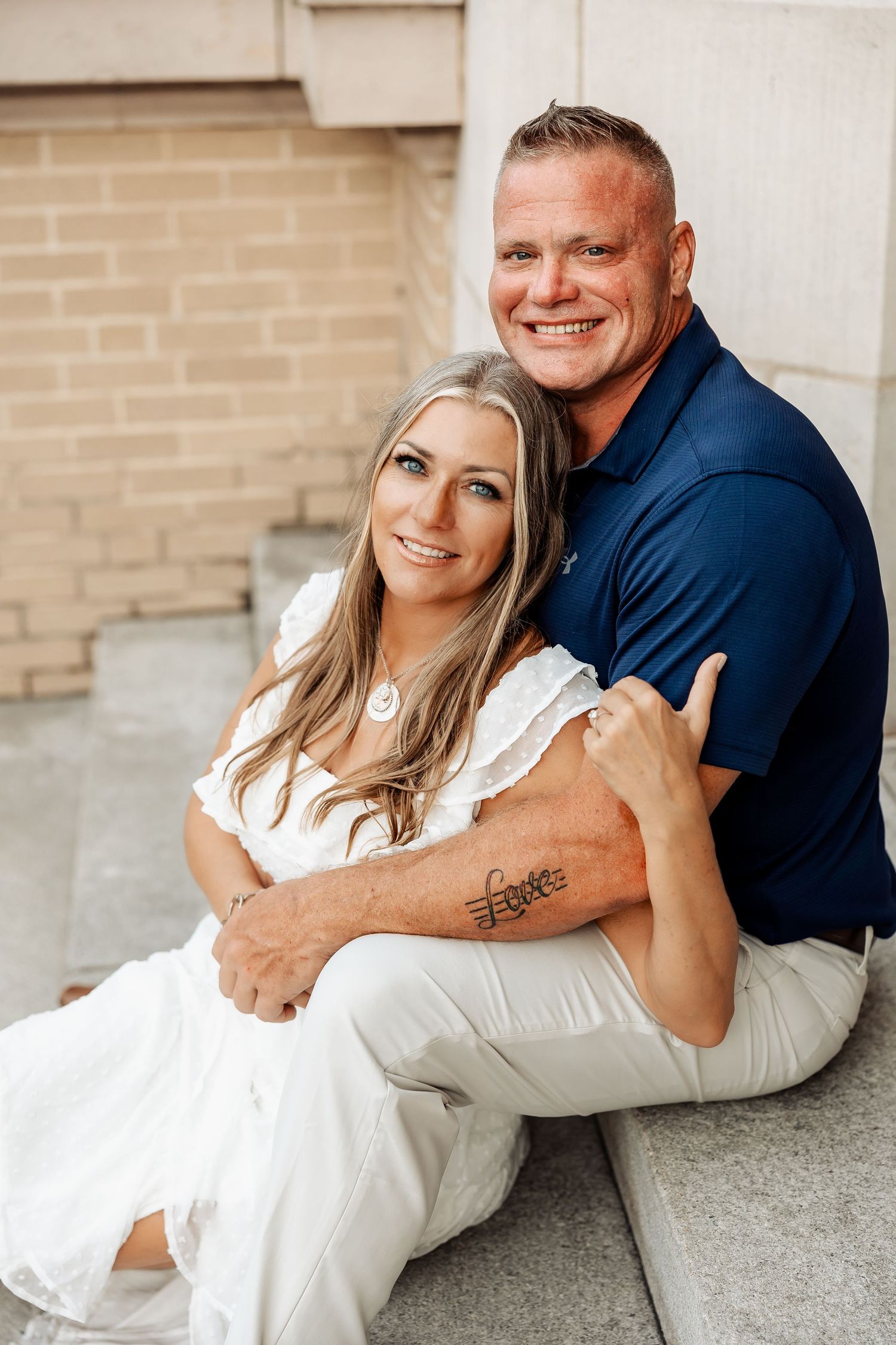 Smiling couple sits closely together on stone steps in a warm outdoor portrait session.