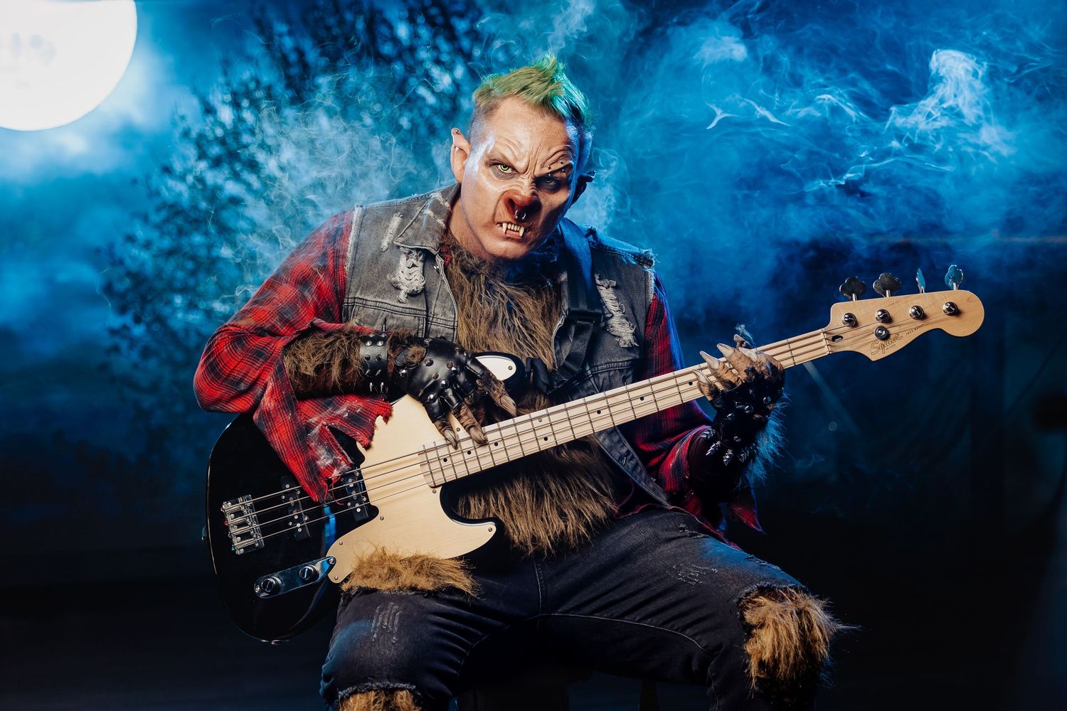 Werewolf costume performer playing bass guitar under dramatic moonlit blue stage backdrop with fog effects.