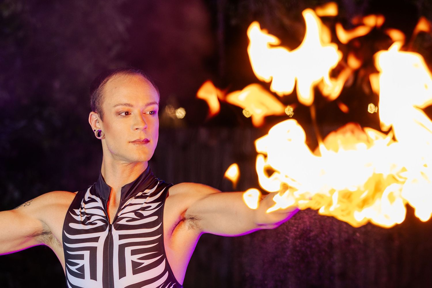 Female fire performer in tribal bodysuit poses with large flames behind her during a nighttime show.
