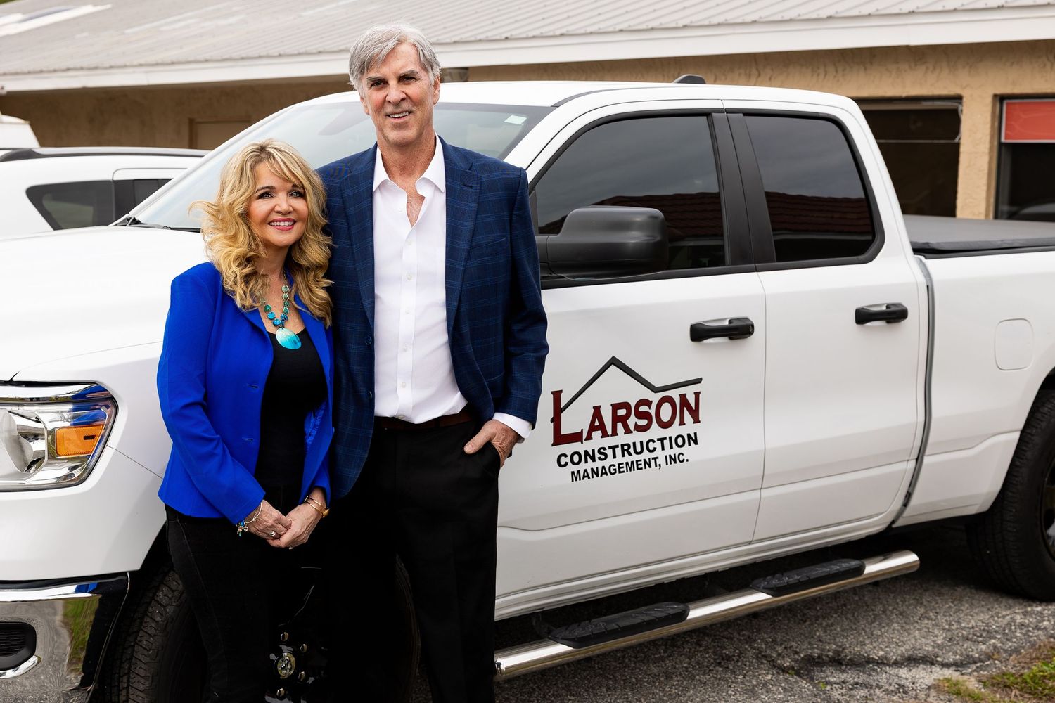 Man and woman posing in front of a white Larson Construction Management truck.