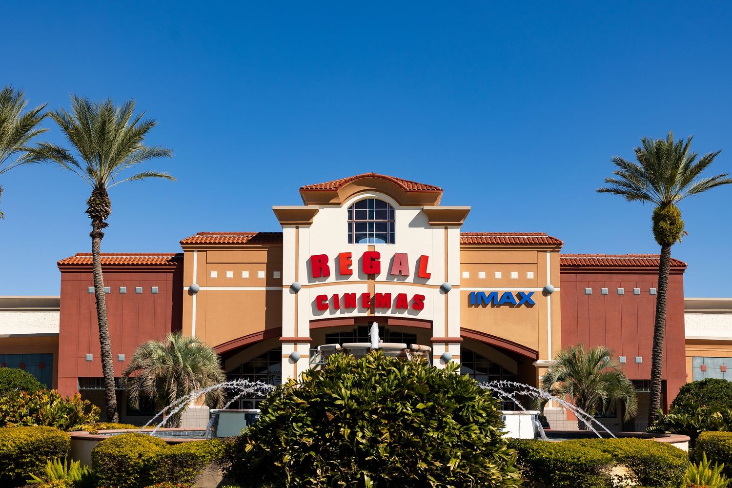 Close-up of Regal Cinemas IMAX theater facade surrounded by lush palm trees and blue sky.