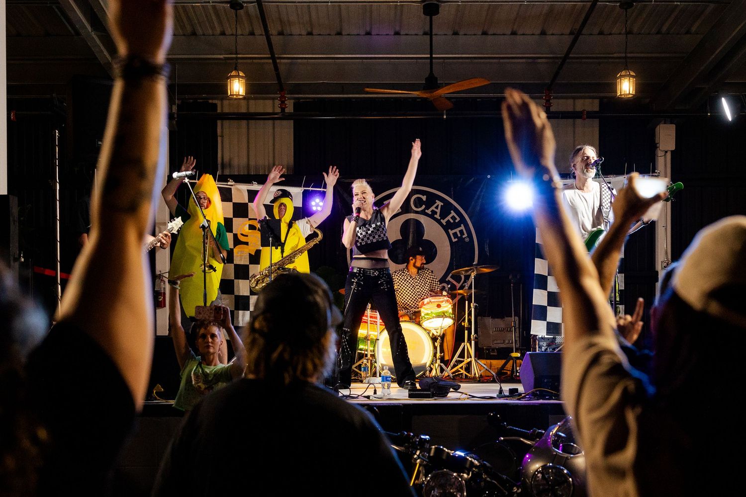Crowd raises hands toward energetic band performing on stage with female vocalist at live concert.