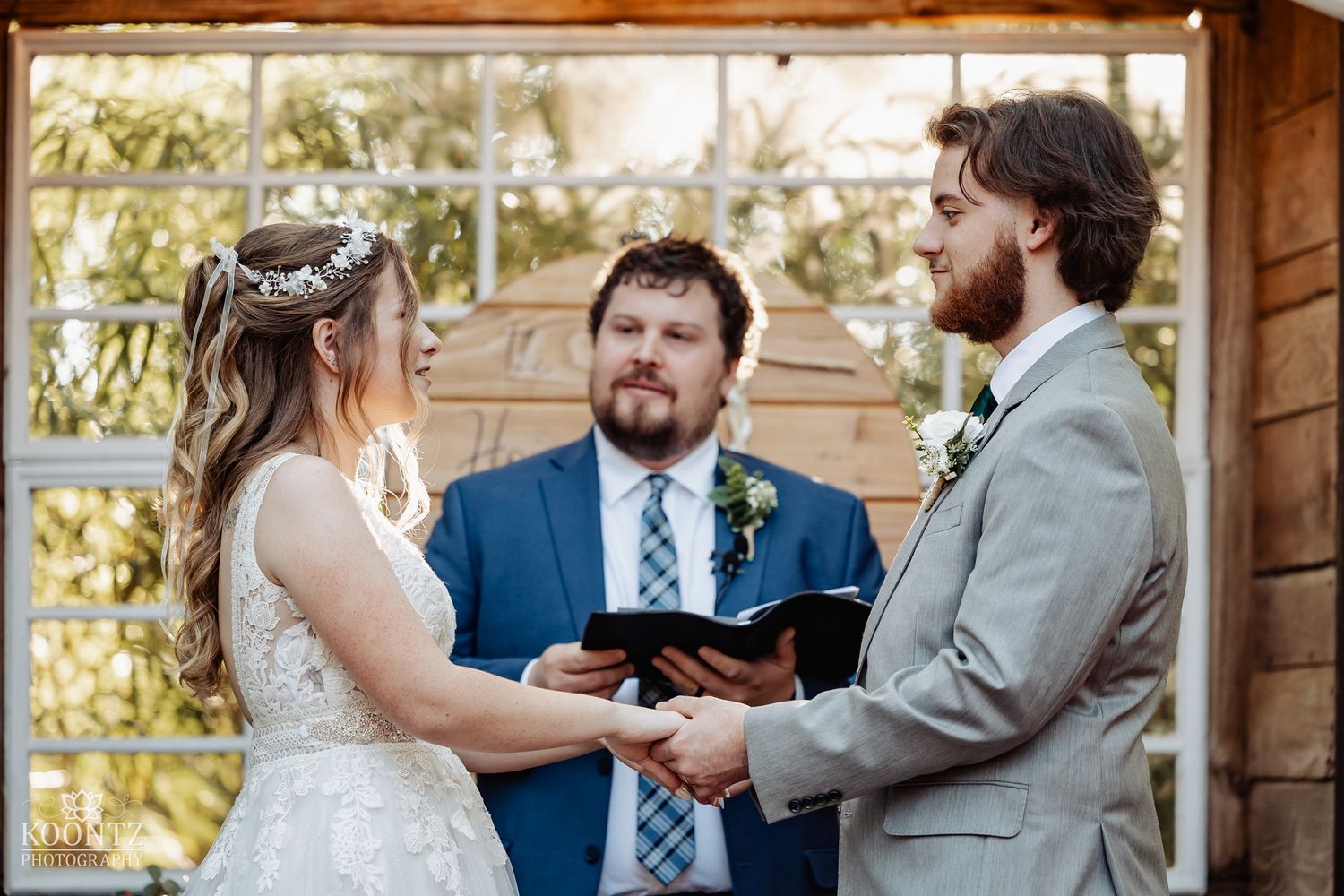 Bride and groom exchange vows before officiant at rustic wooden altar during outdoor forest wedding.