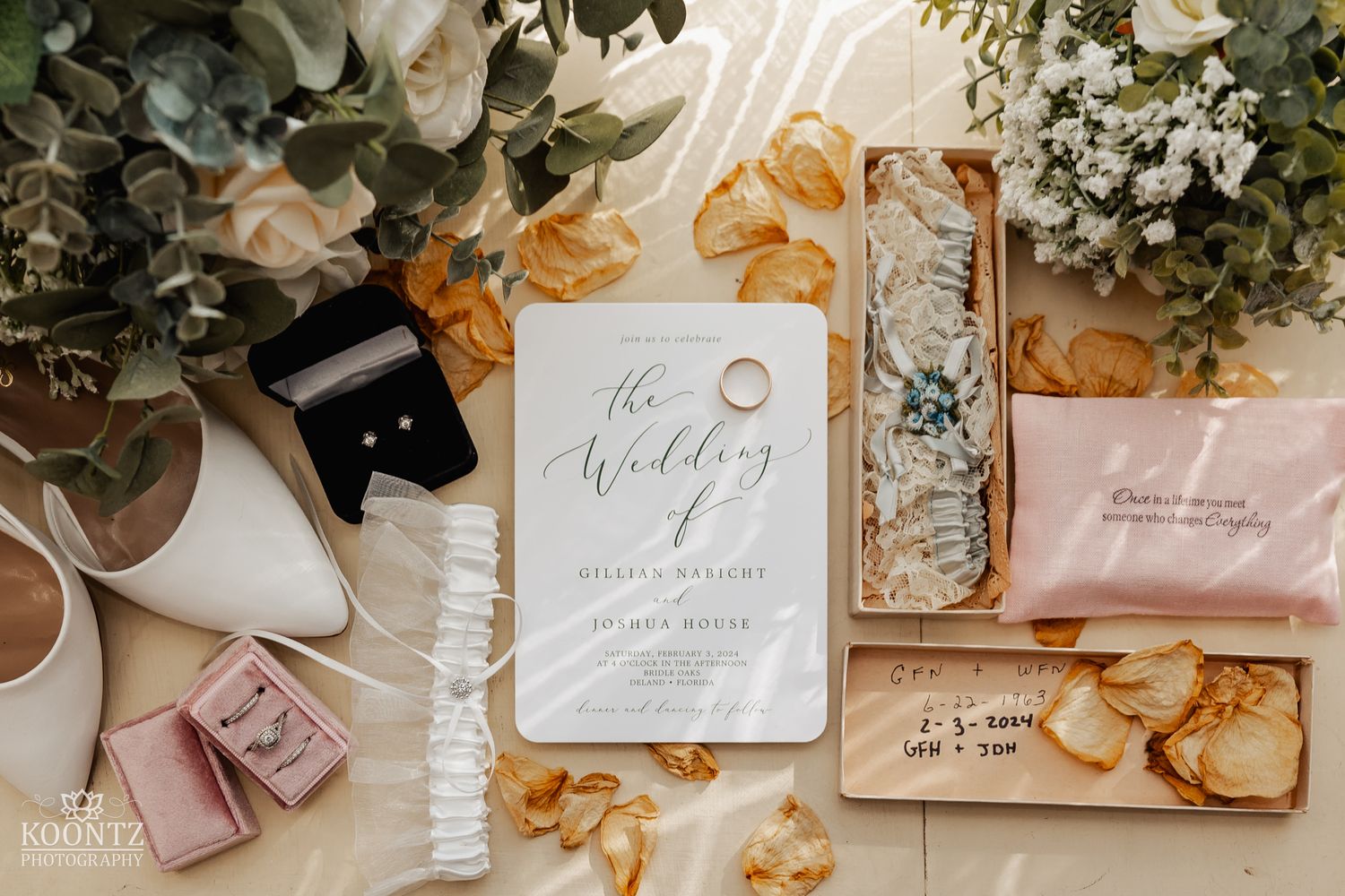 Elegant wedding flat lay featuring invitation suite, rings, bridal accessories, and floral arrangements.