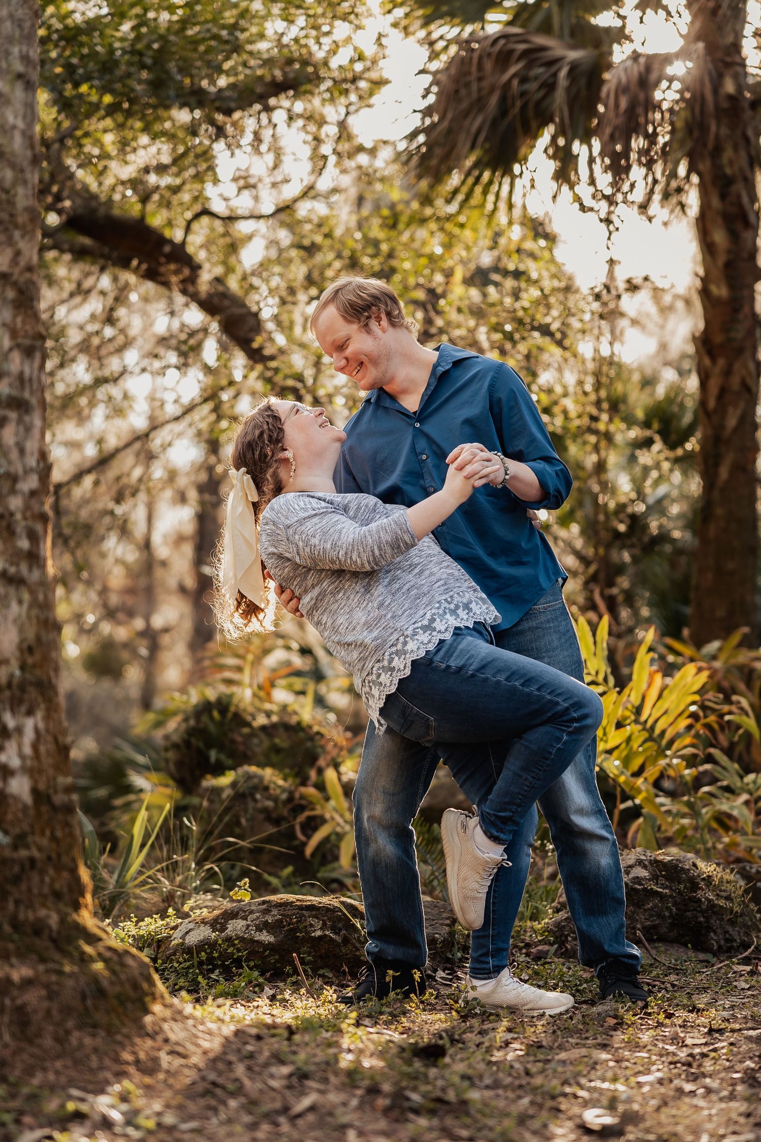 Couple dancing and laughing together in a sunlit forest with lush green ferns.