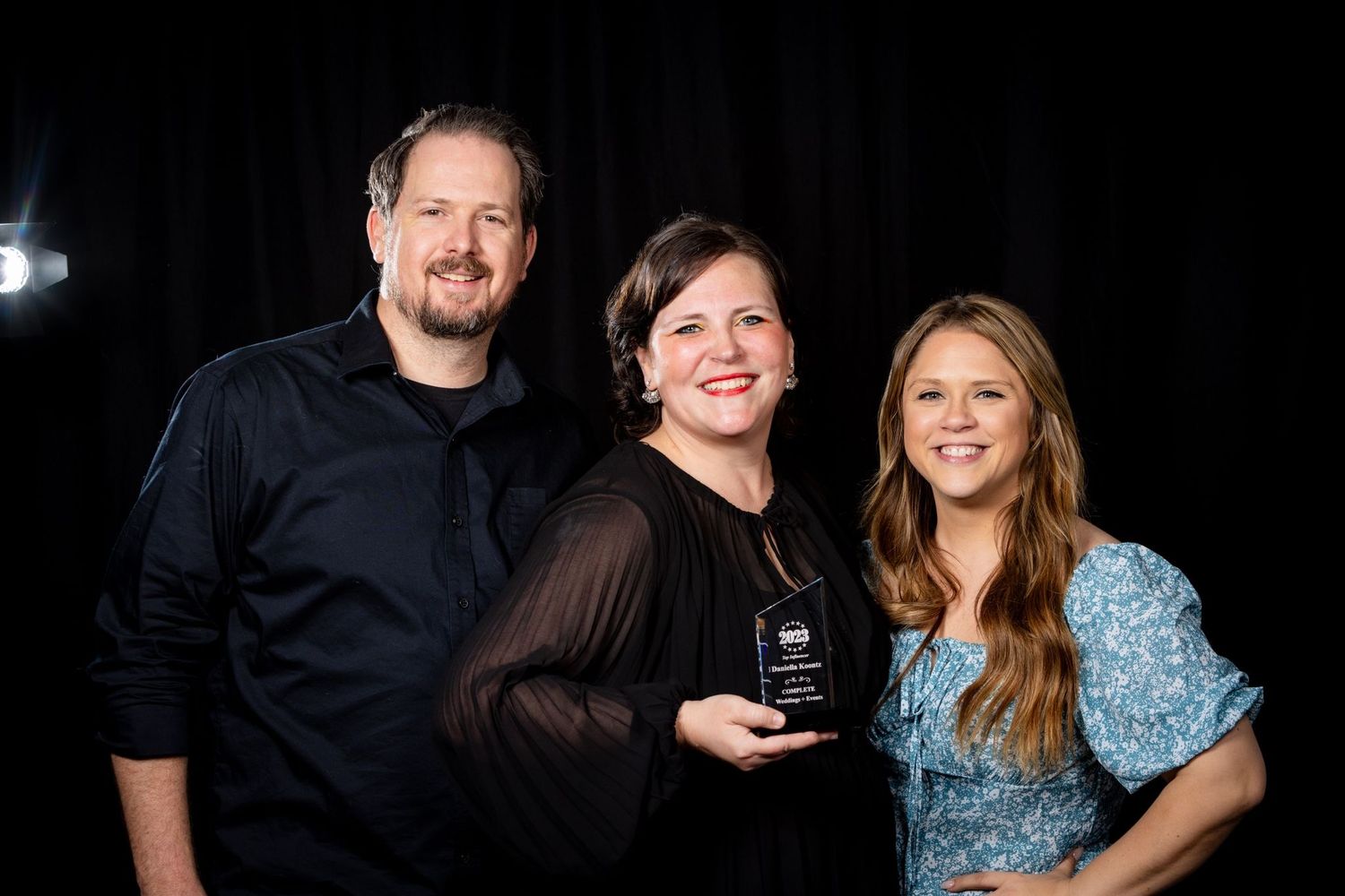 Award ceremony group photo with three people against black background holding trophy.
