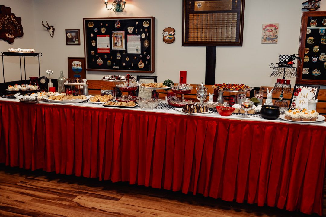 Long banquet table with red tablecloth displaying various desserts and treats.