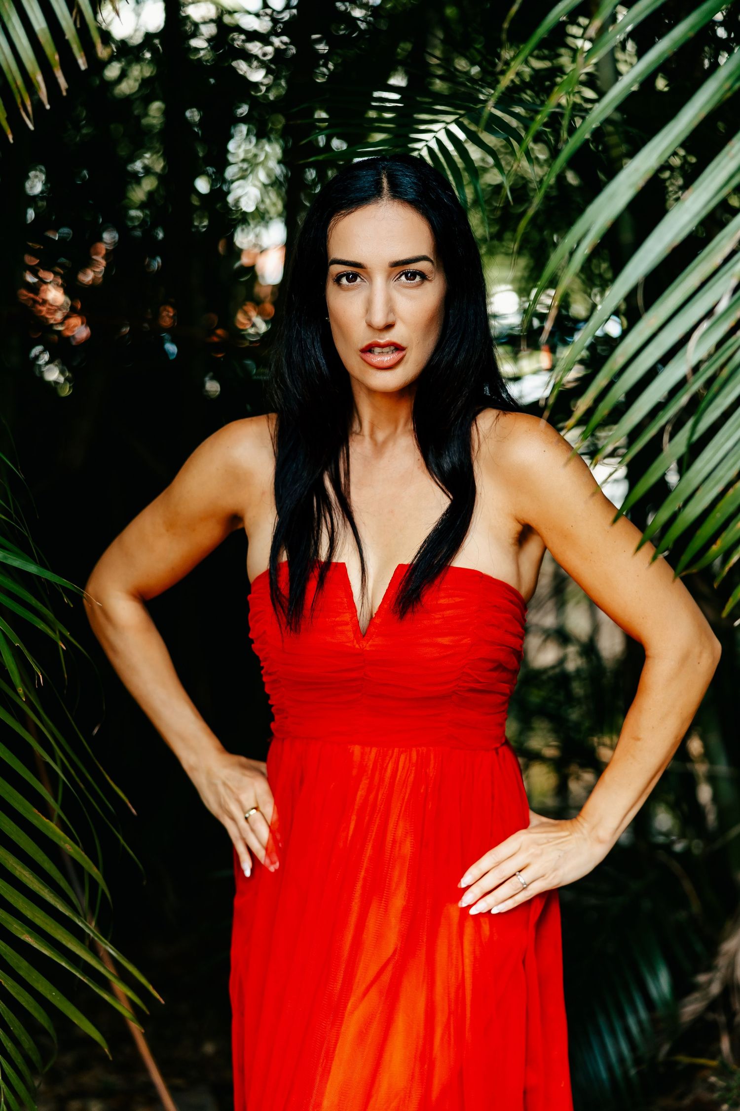 A dramatic portrait in a tropical setting featuring a red flowing dress against palm fronds.