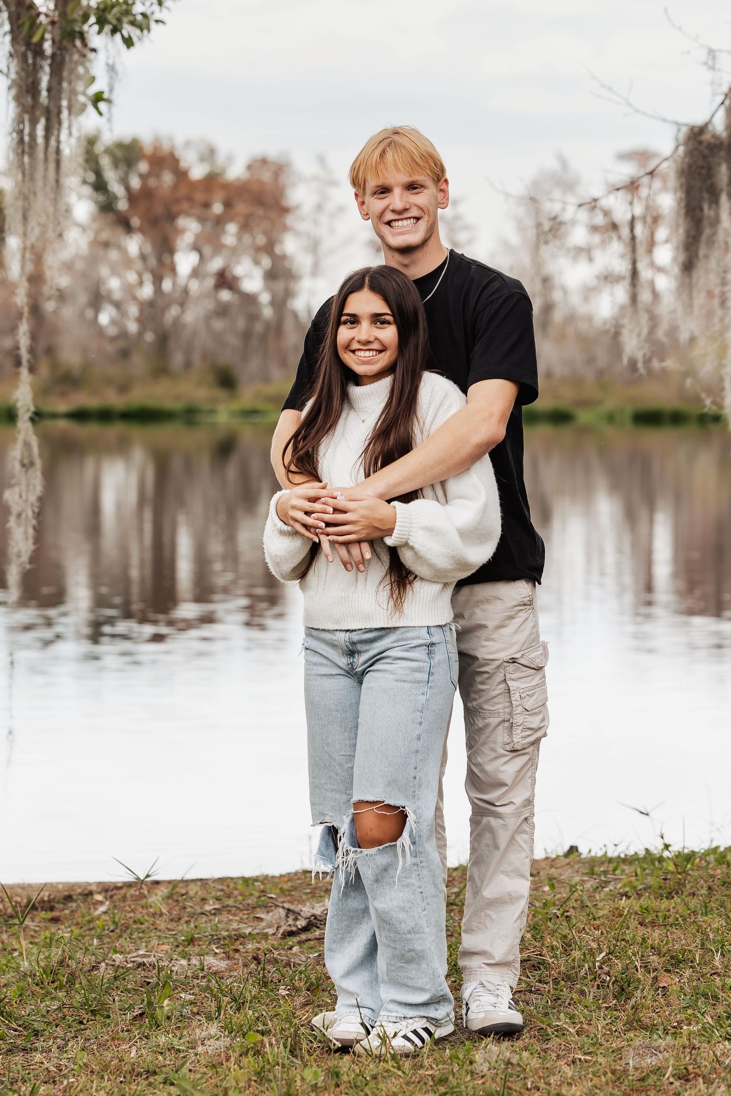 Young couple embracing and smiling together by a tranquil lake surrounded by autumn trees.