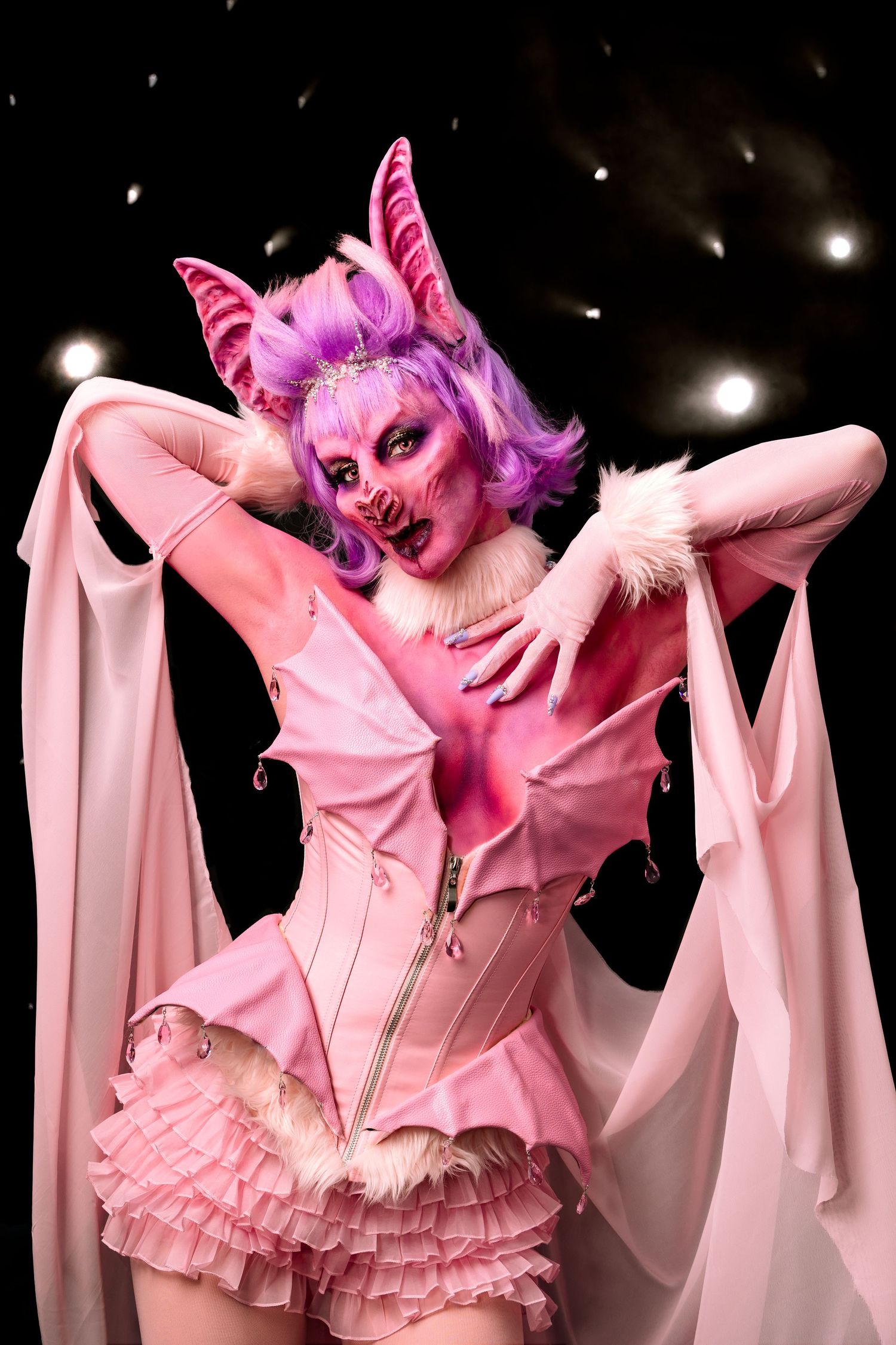 Pink cosplay performance featuring dramatic lighting and butterfly-inspired headpiece on dark stage.