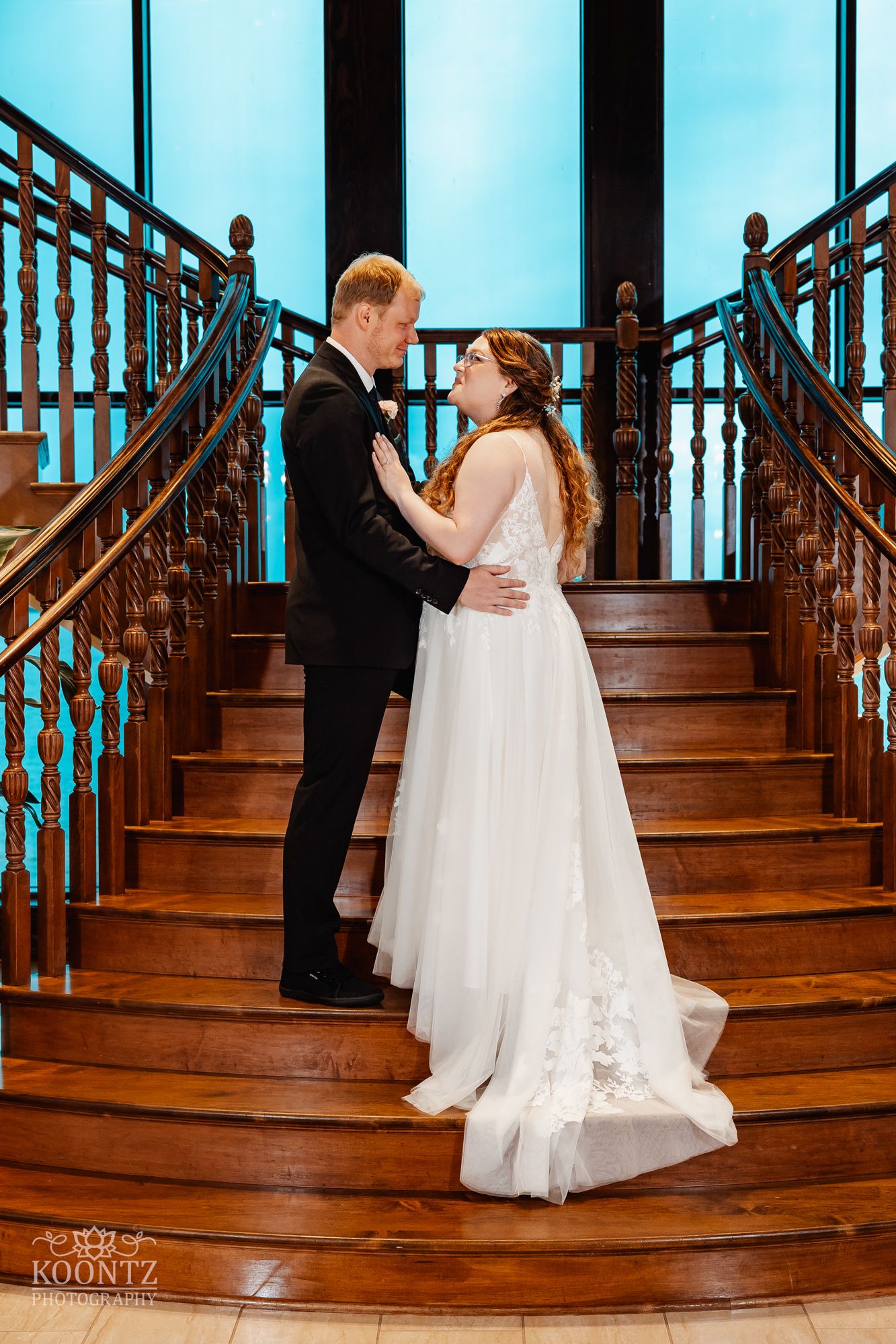 Romantic wedding pose on wooden staircase with turquoise backdrop.