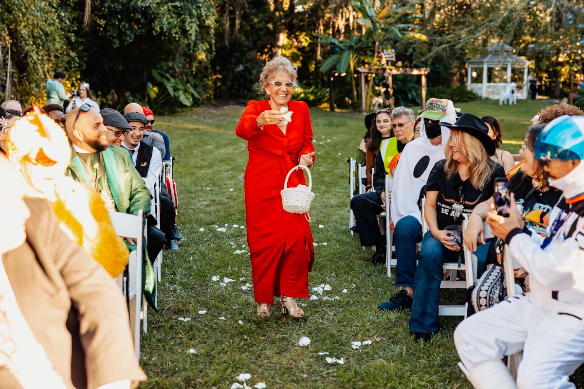 A Halloween costume party outdoors with guests seated on chairs watching a person in red addressing the group.