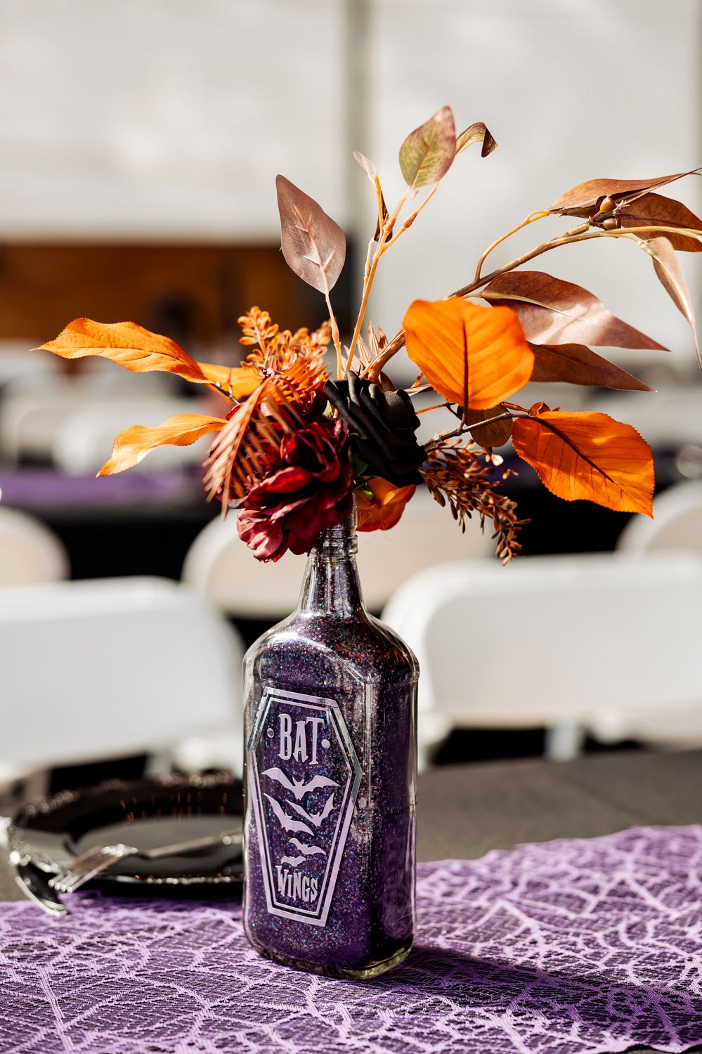 Purple Halloween-themed bottle vase with orange and burgundy fall foliage arrangement.