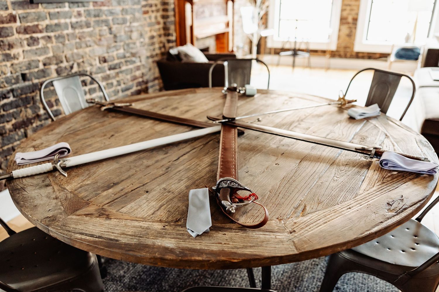 Medieval swords and leather belt arranged decoratively on rustic wooden round table in industrial brick interior.