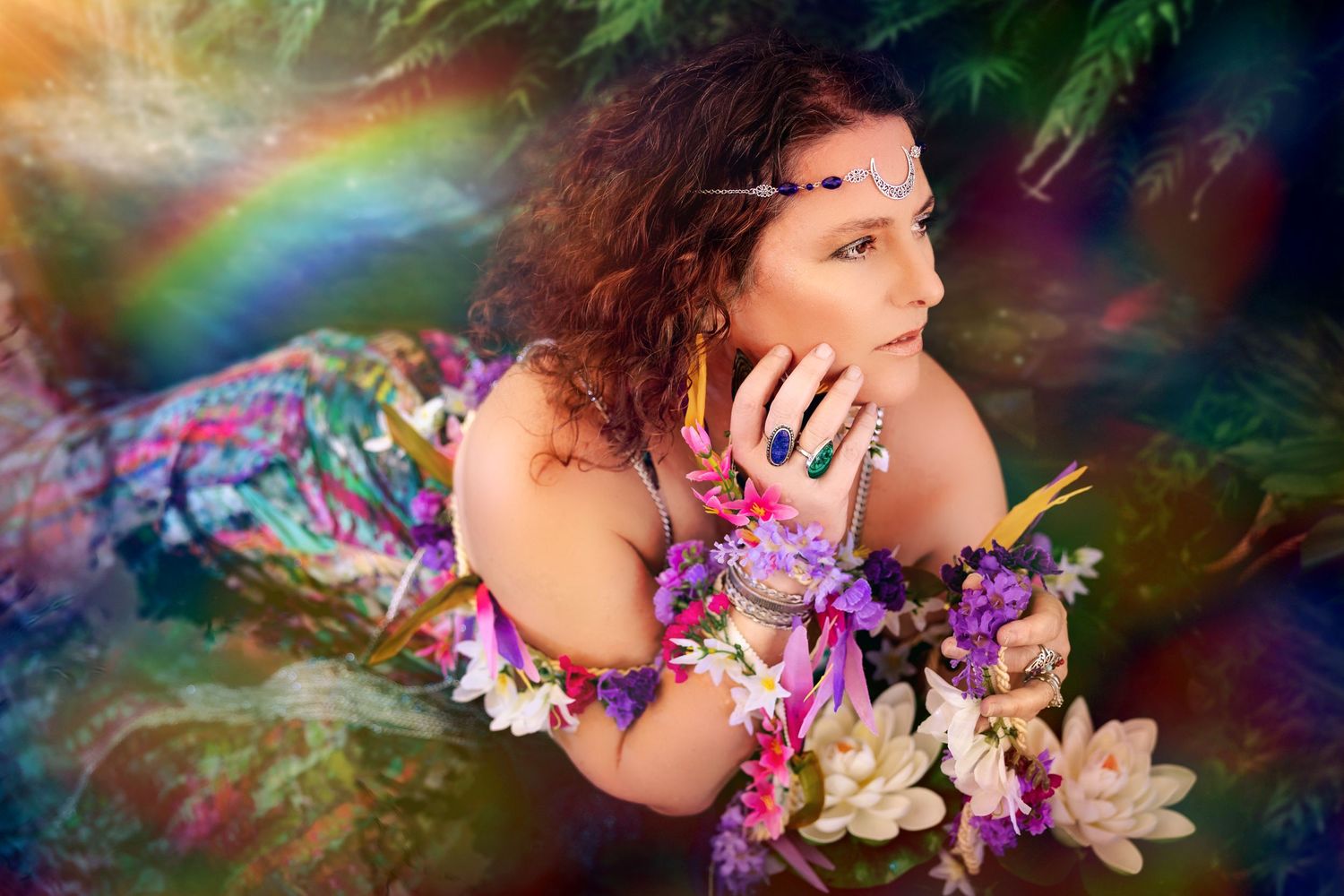 Woman with curly hair adorned with flowers and colorful jewelry poses in a magical rainbow forest setting.