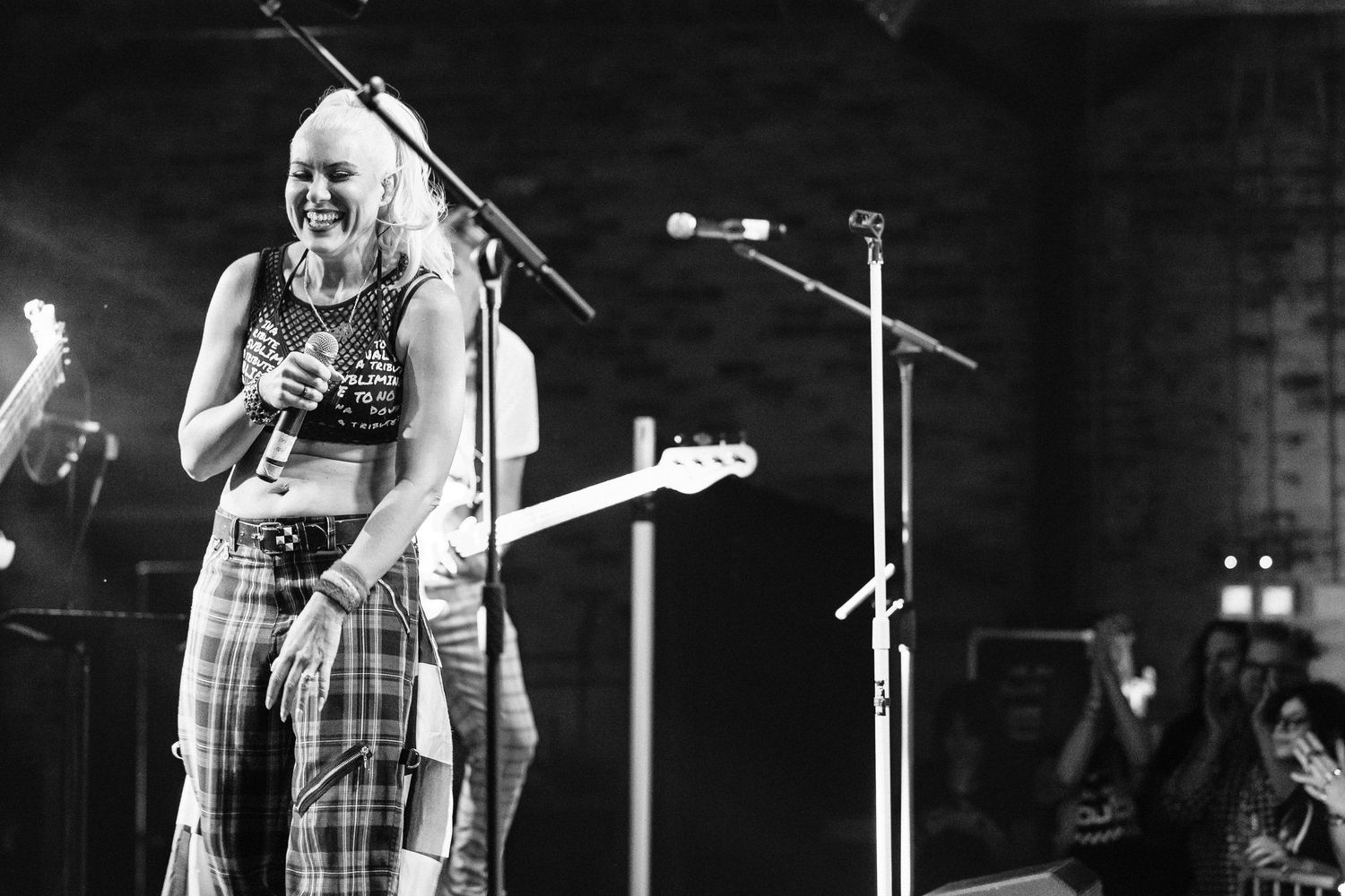 Black and white photo of smiling female vocalist performing on stage with guitarist in background.