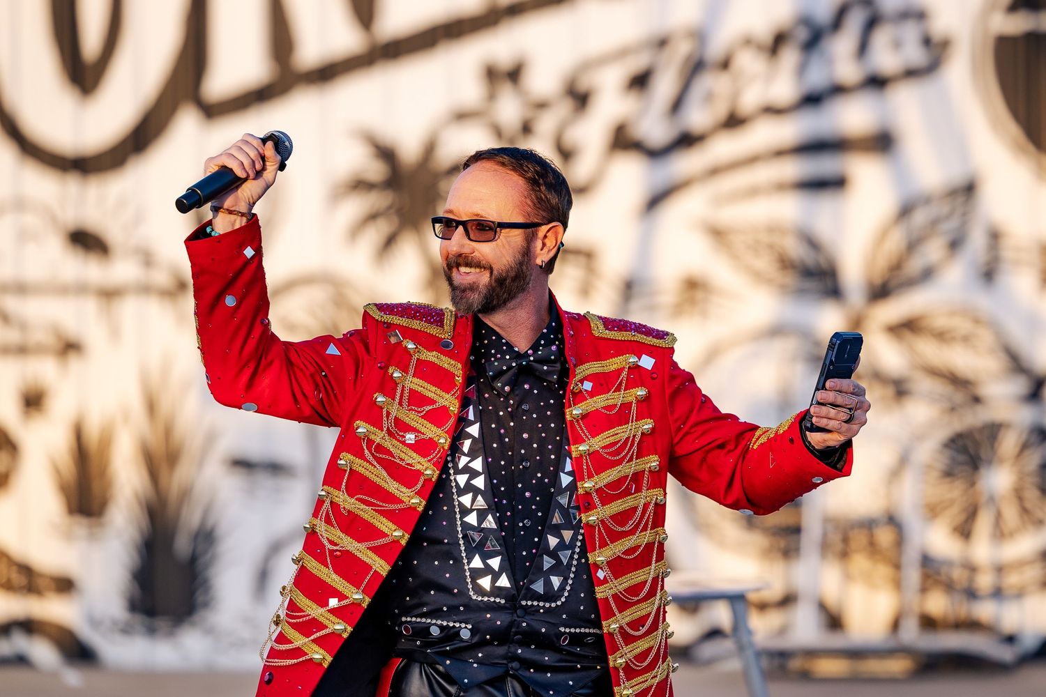 Smiling emcee in red military jacket holding microphone at an outdoor Orlando Florida circus performance.