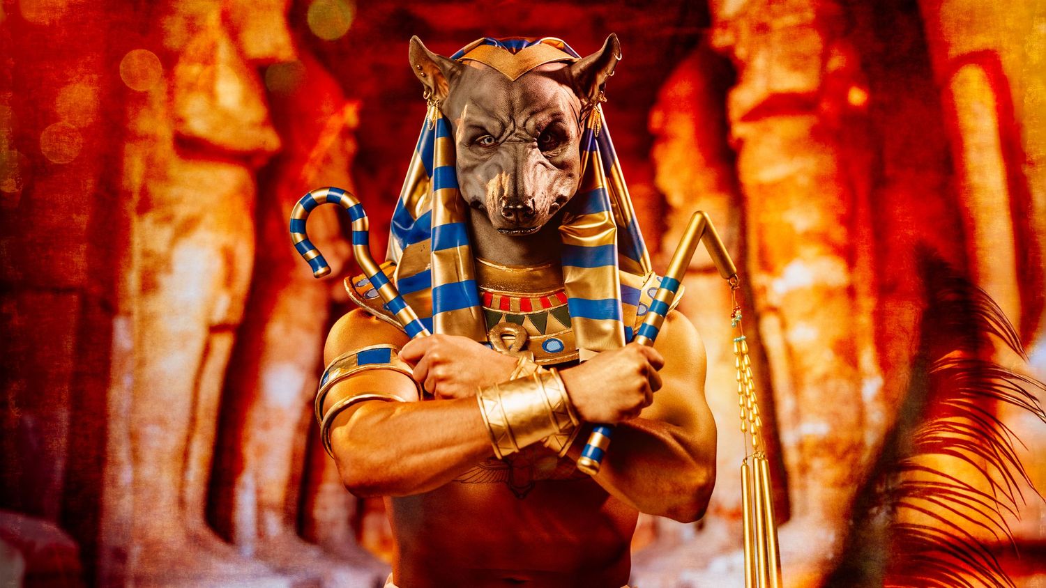 Person dressed as Egyptian deity Anubis in golden accessories and white linen in temple setting.