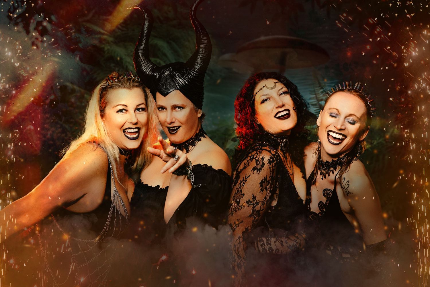 Four women in dark fantasy Halloween costumes including Maleficent horns laughing together.
