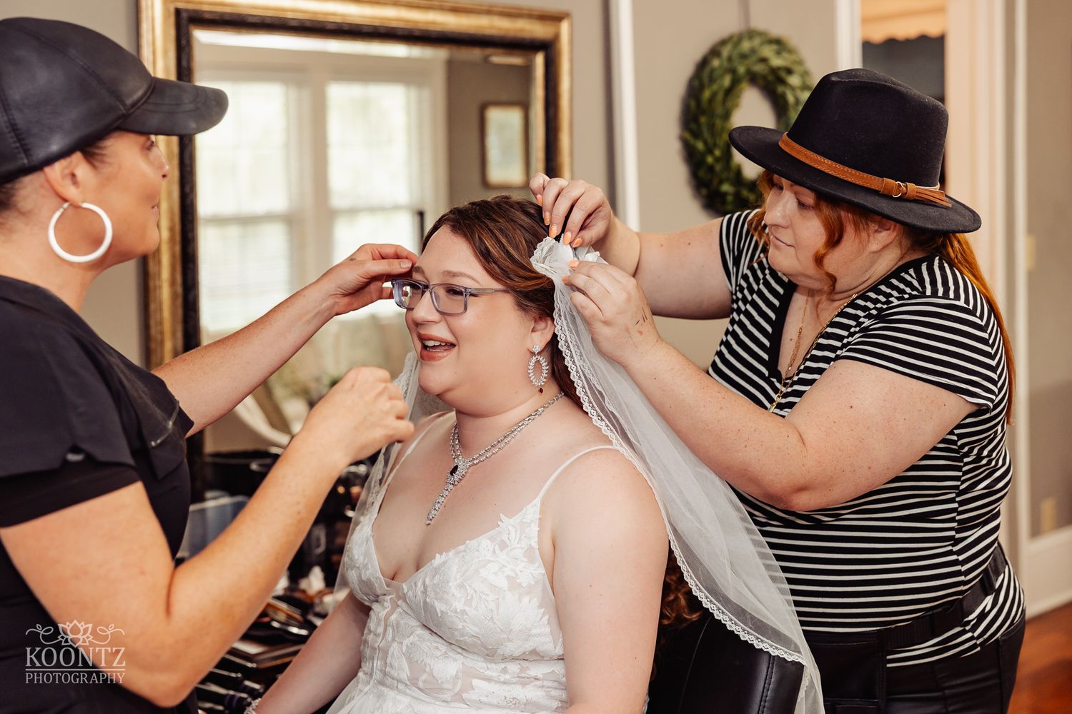 Wedding preparations show styling team helping attach a bridal veil in a warm indoor setting.
