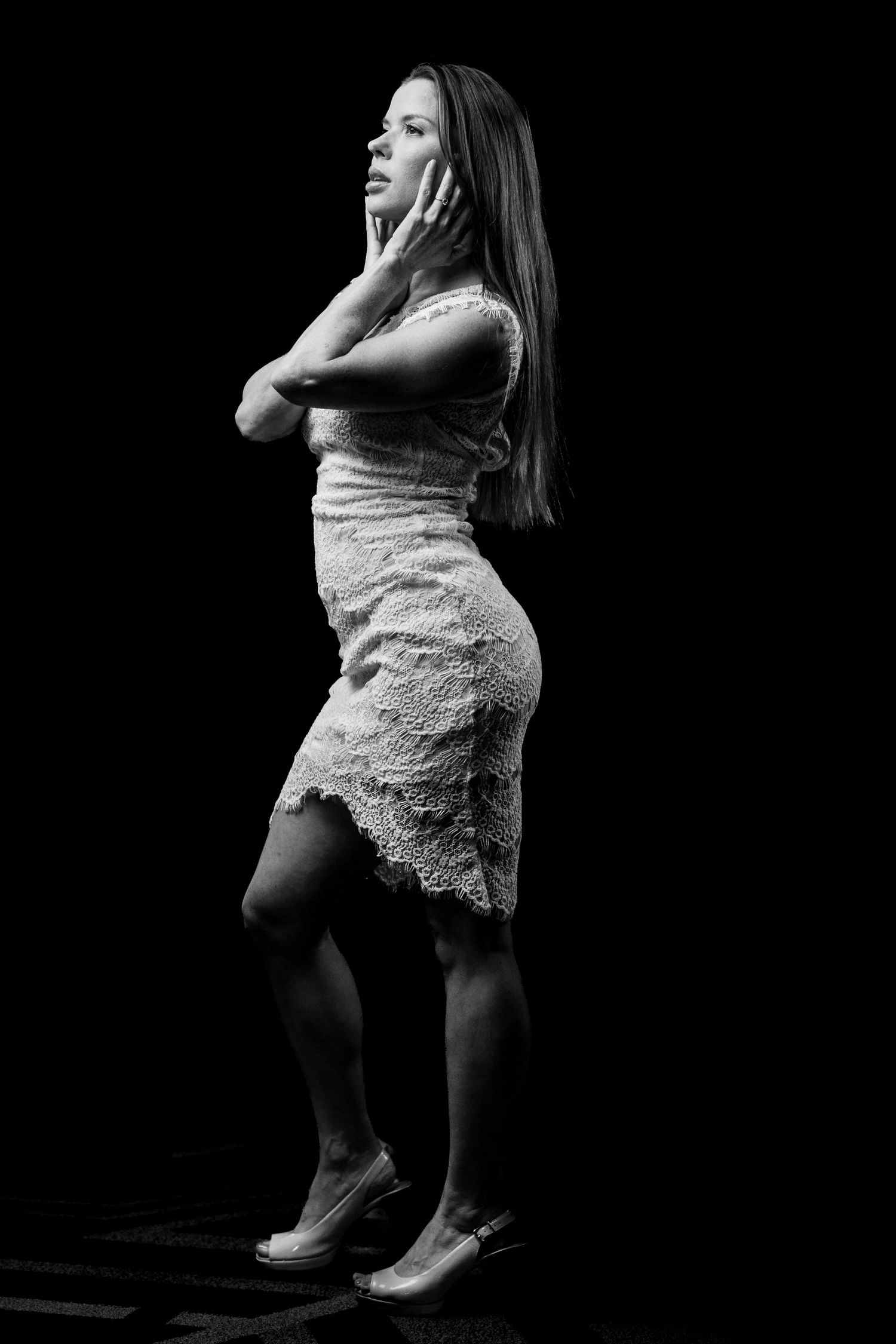 Artistic black and white portrait of someone in a lace dress striking a dramatic pose against dark background.