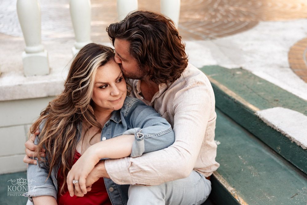 Intimate moment between couple sitting on green bench in casual denim and white attire.