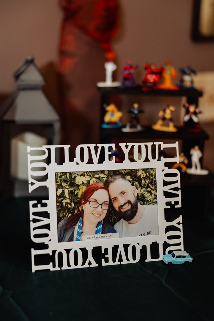 A white 'Love You' picture frame with decorative figurines in the background.