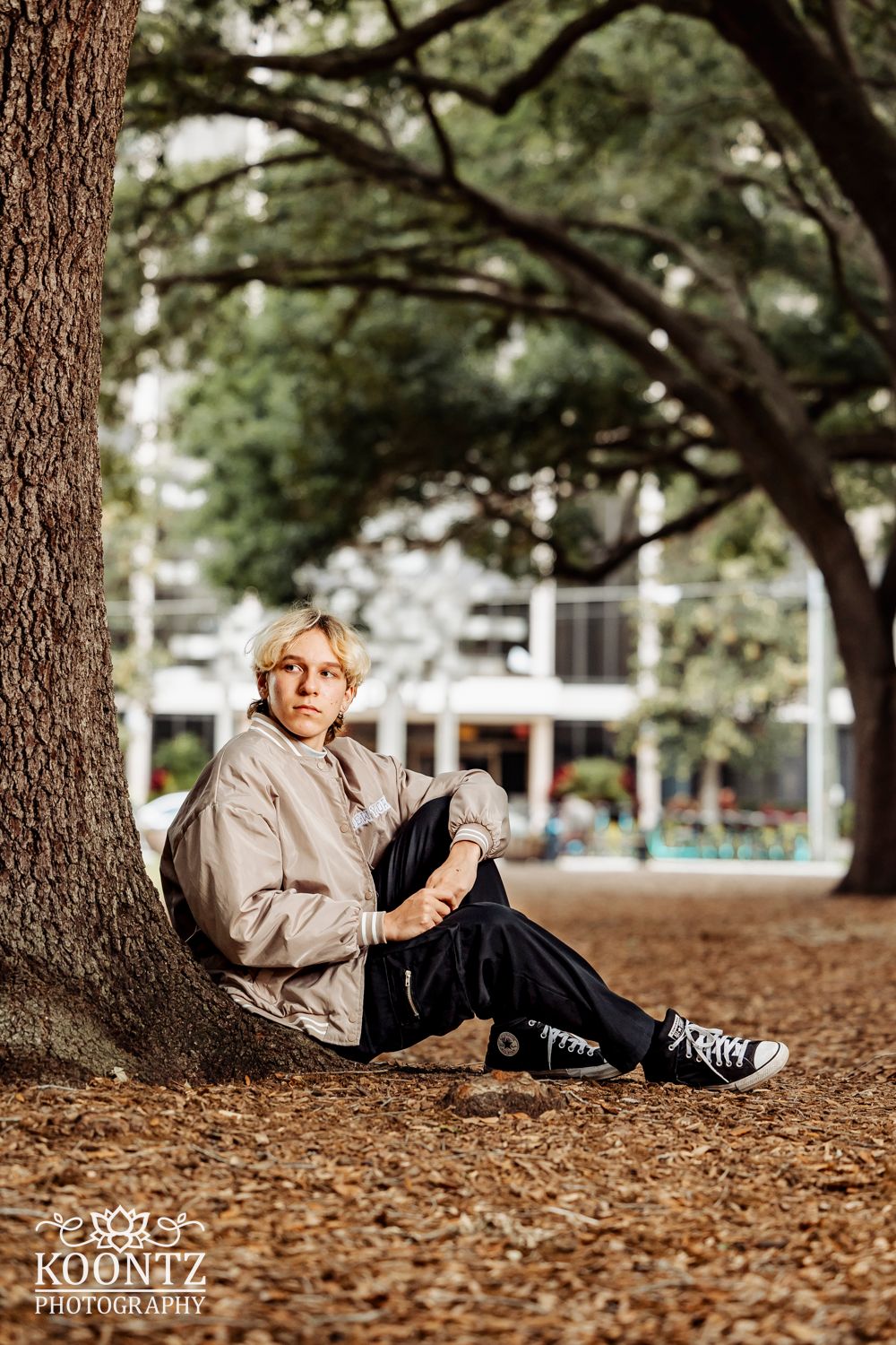 Outdoor portrait against a large tree trunk in an urban park setting.