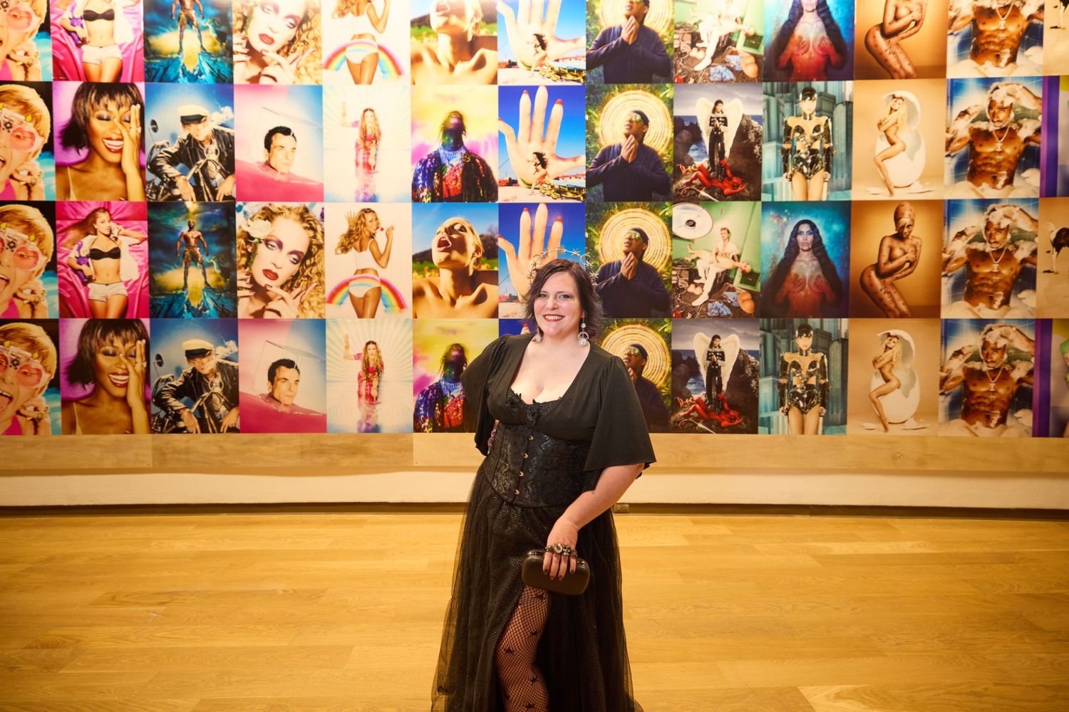 A person in a black outfit performs a dance move against a wall covered in colorful photographs.