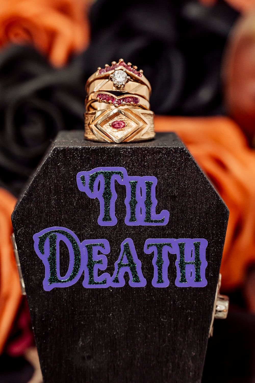 Gold and ruby wedding rings stacked on a black coffin-shaped display reading 'Til Death'.