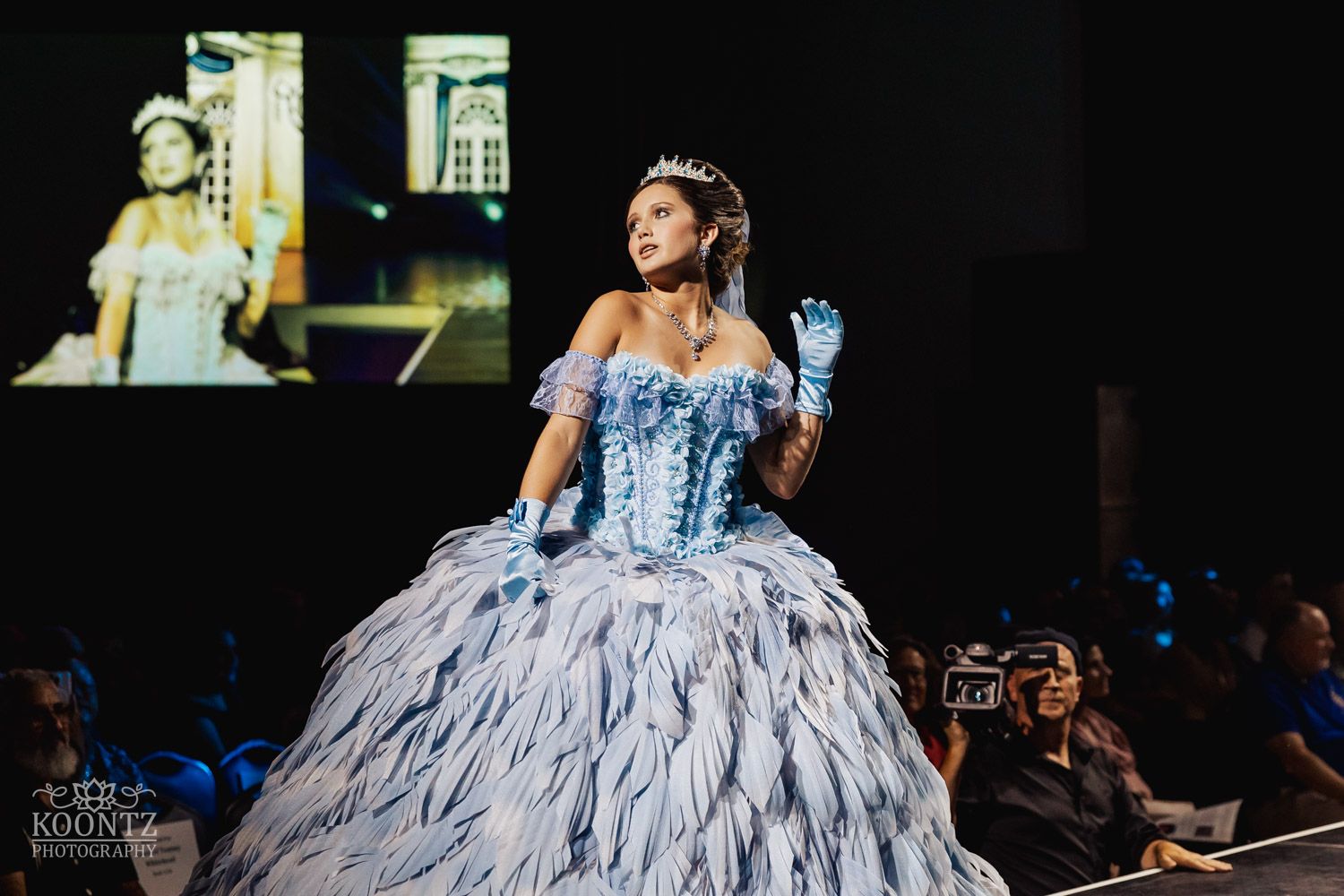 Fashion model wearing an elegant white ballgown with dramatic ruffled skirt performs on a dark runway.