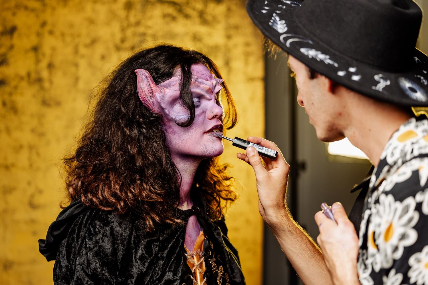 Behind the scenes photo showing makeup application on performer against yellow background.