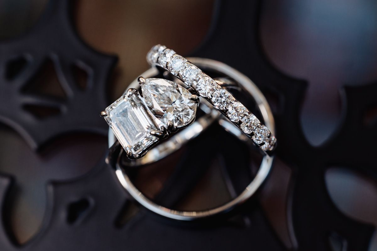 Close-up of elegant diamond engagement ring and wedding bands displayed on a decorative dark surface.