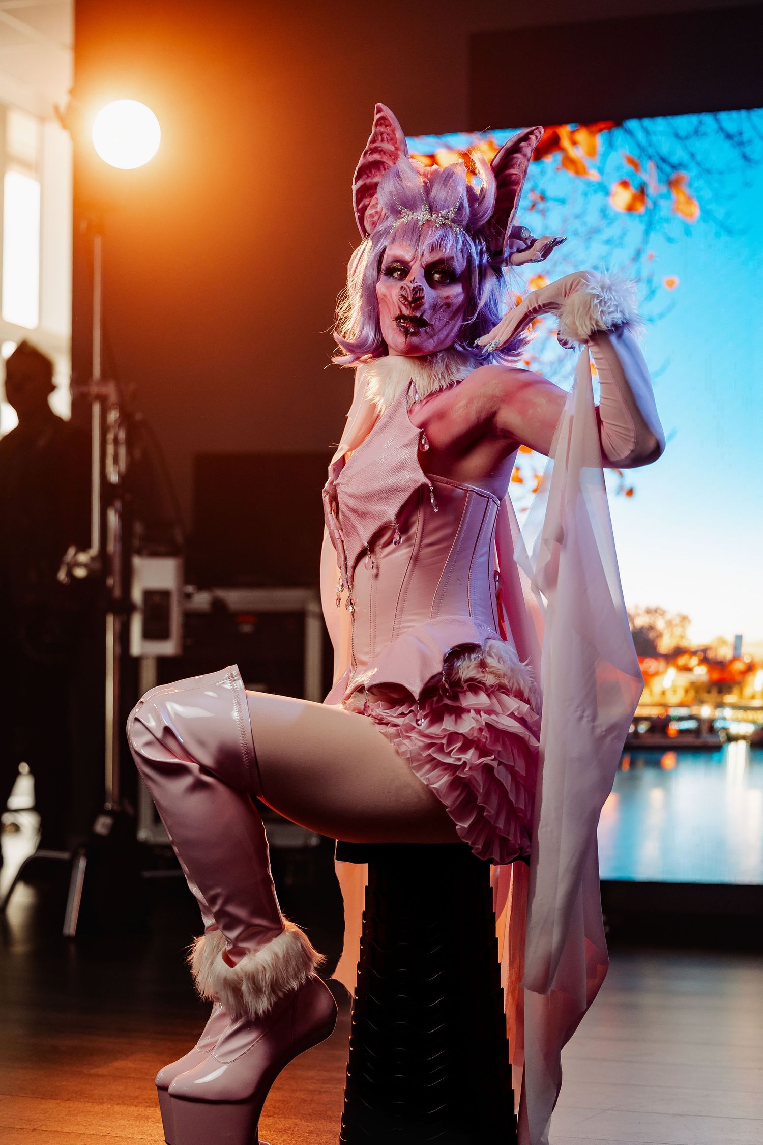 Person in pink demon cosplay costume with horns and scary mask posing on stage under dramatic lighting.