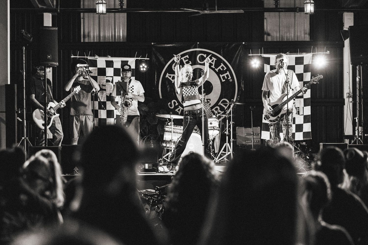 Rock band performs on stage in black and white photo before large crowd.
