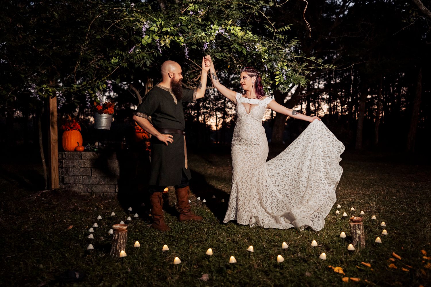 An outdoor wedding celebration with string lights features a dancing couple surrounded by glowing candles on the ground.