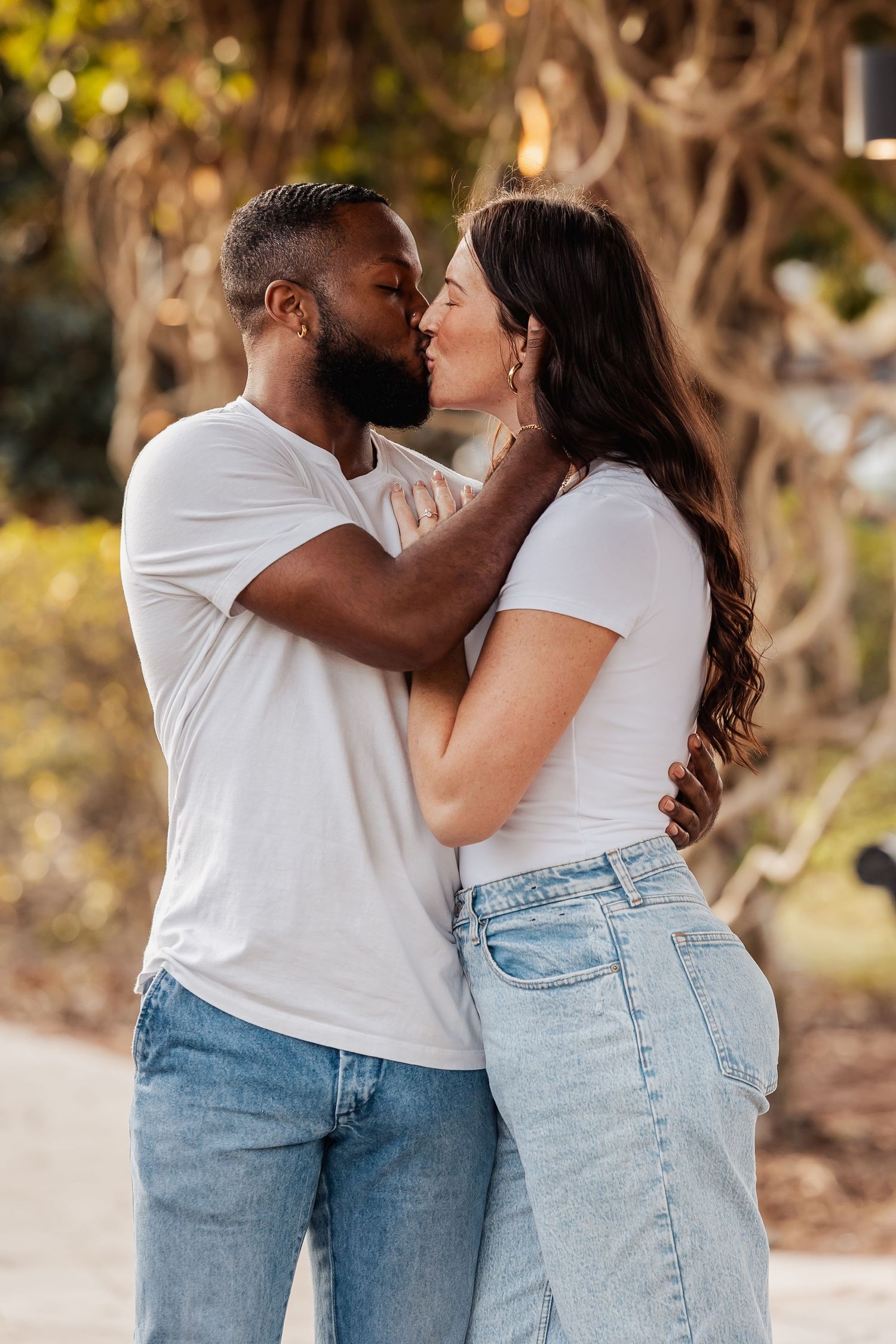 A tender moment between a couple in white shirts and blue jeans sharing an intimate embrace outdoors.
