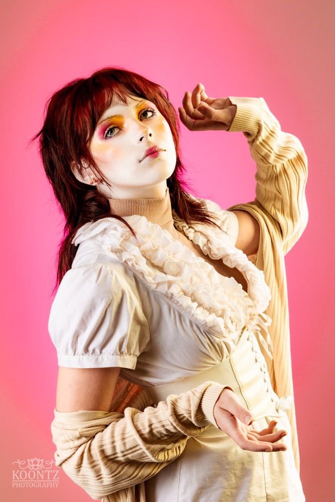An artistic portrait with dramatic lighting showing Victorian-style fashion against pink background.