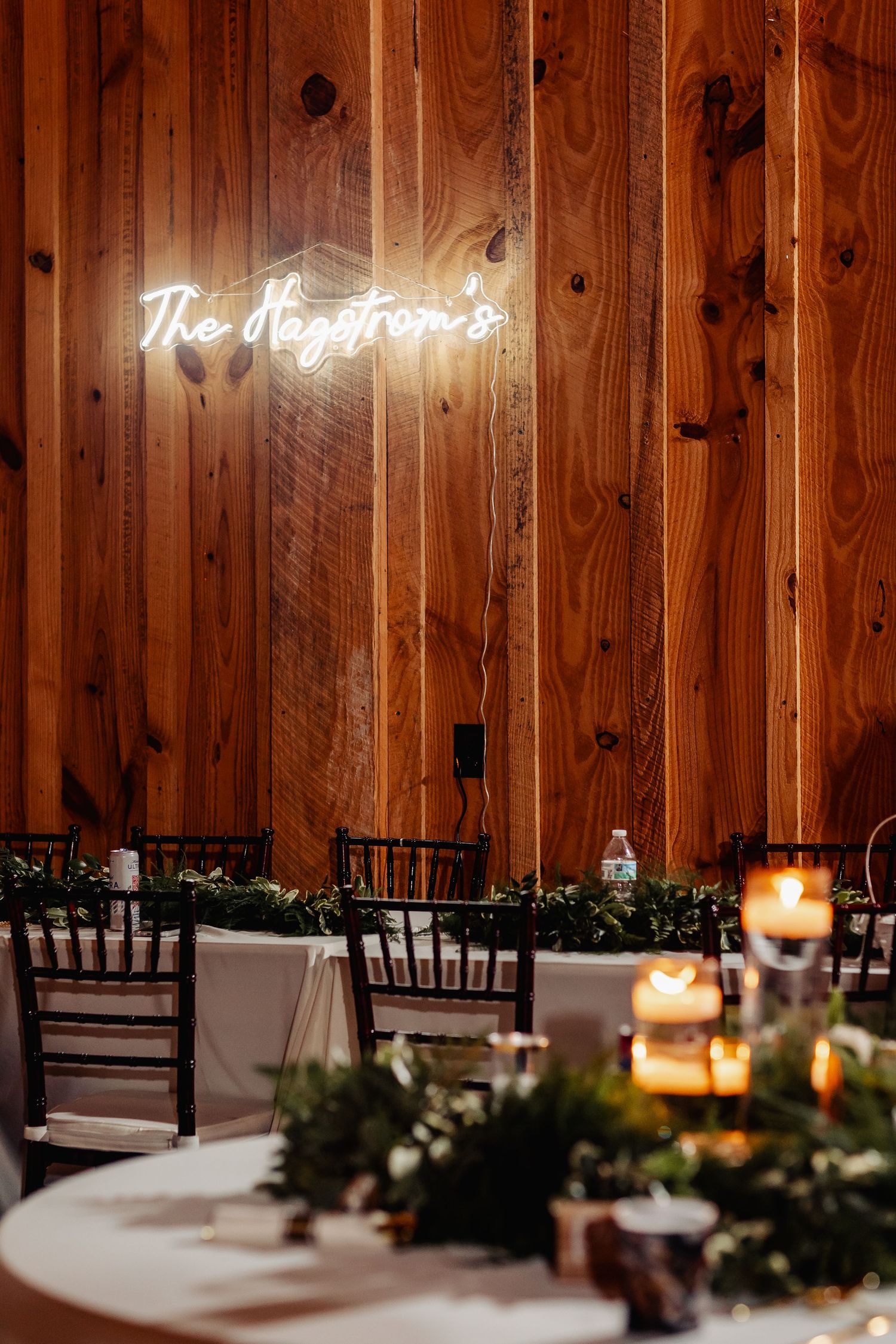 Rustic wooden wall with neon sign and elegant wedding table decor with candles and greenery.