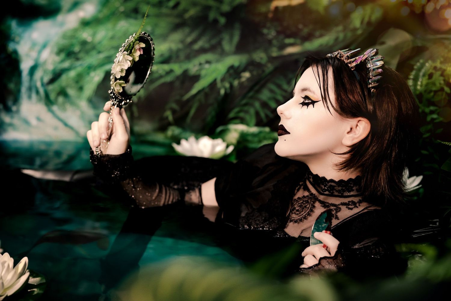 Dark gothic woman in black lace holding ornate mirror in mystical lily pond setting.