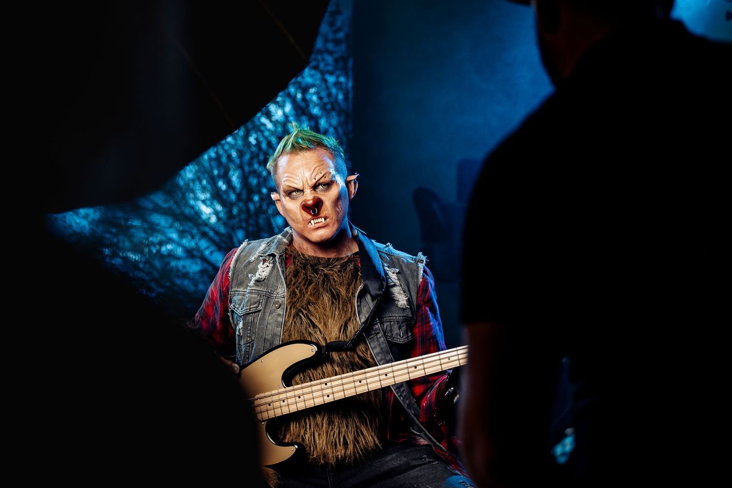 Performer in medieval-style costume plays stringed instrument against dark blue backdrop.